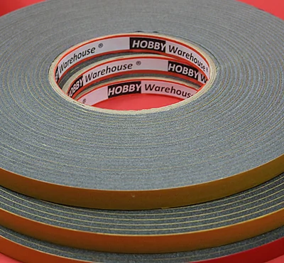 Foam Tape (grey) on cardboard roll on a red background.
